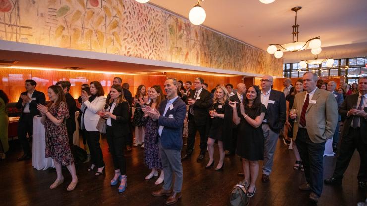 A crowd of adults stand in a room clapping.